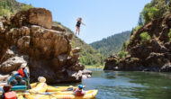 A woman jumps from a cliff into a river where rafts wait
