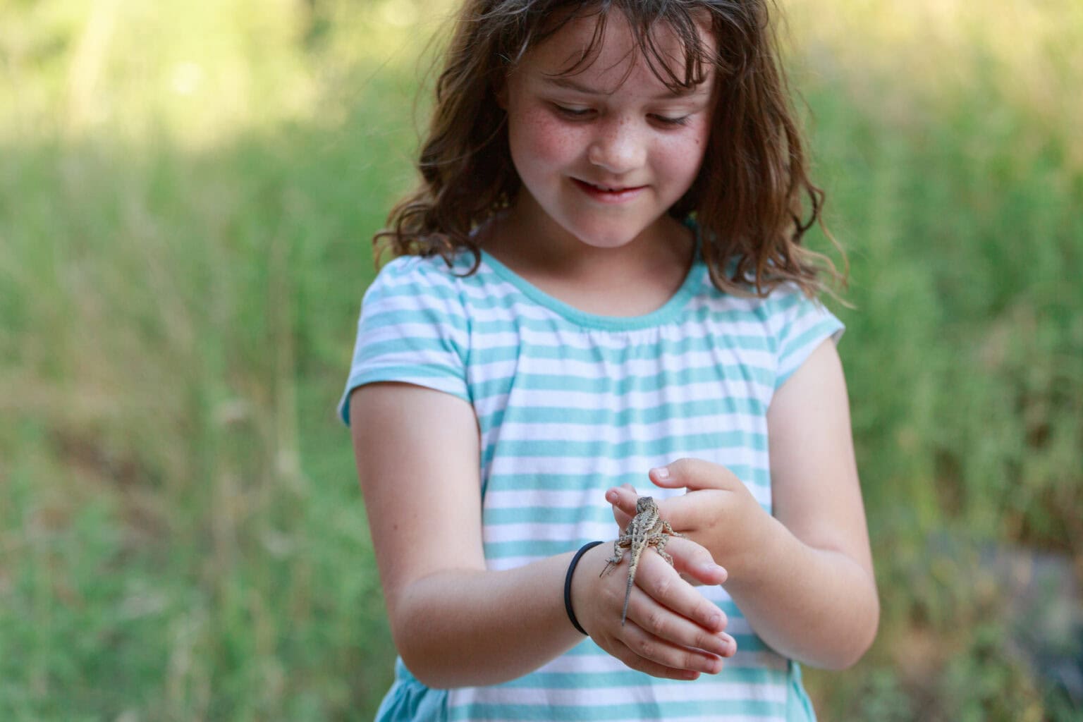 A young girl in a white and blue dress lets a lizard rest on her hand