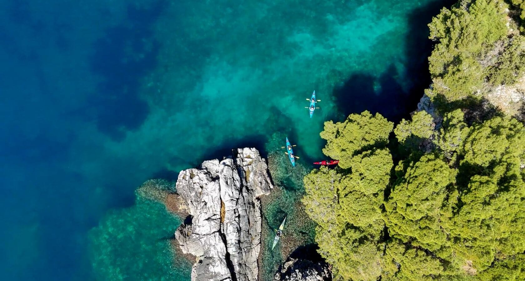 A group of kayakers paddling a craggy shoreline along the Dalmation Coast in Croatia, one of the top sea kayaking destinations in the world.
