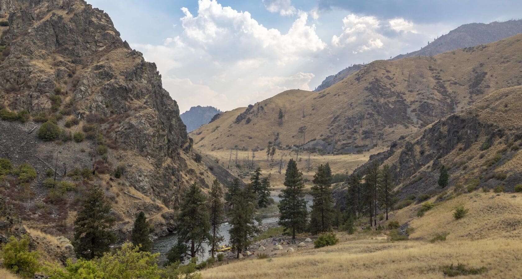 A grassy hillside with tents in the distance alongside a river