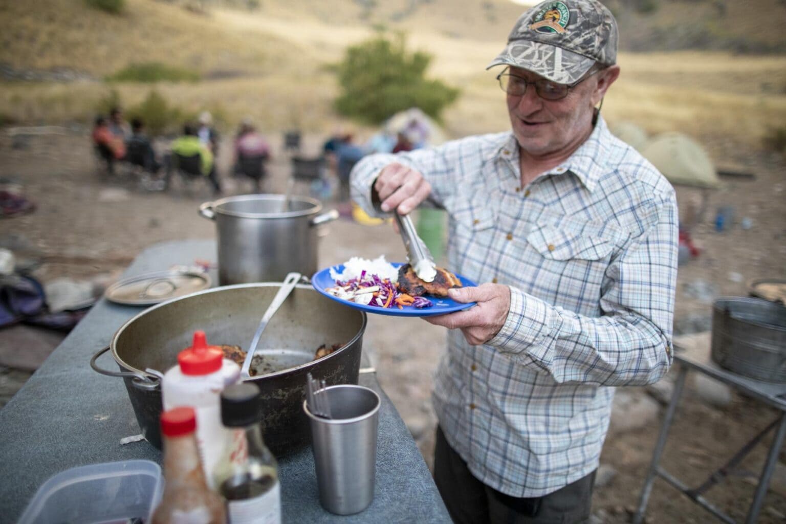 A man in a hat serves himself a plate of food at a campsite along the Salmon River