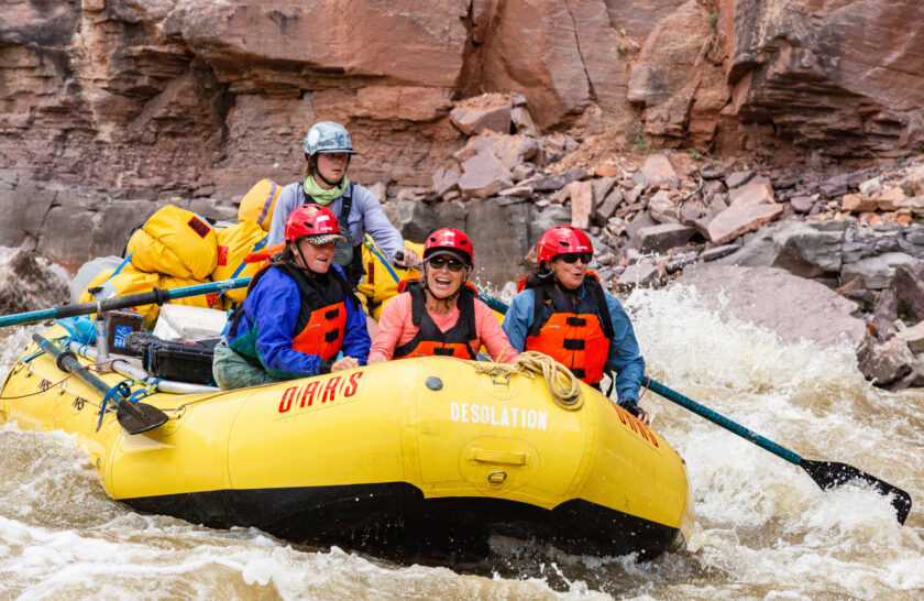 Three women in the front of an oar raft while a guide rows them through rapids on the Yampa River in Utah