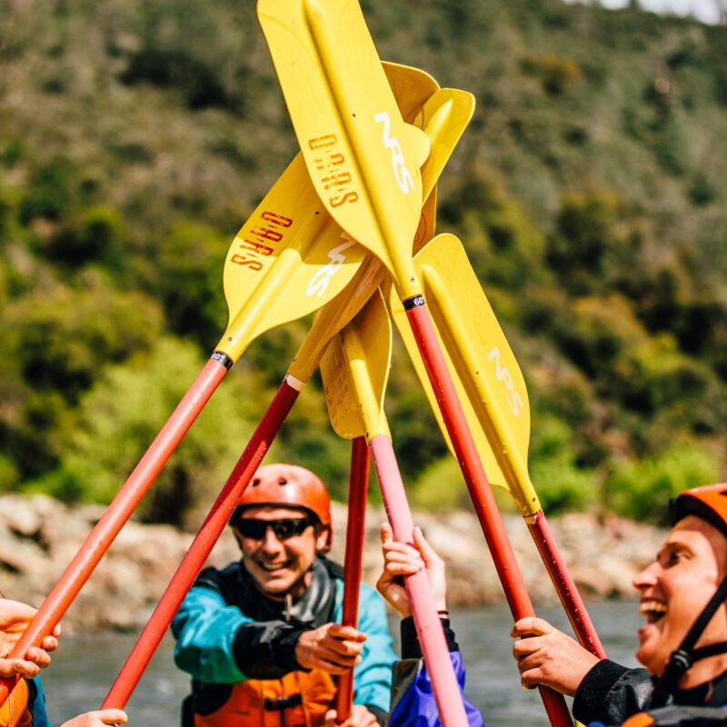 A group of participants in the OARS California Whitewater Guide School celebrates by raising their paddles on the American River.