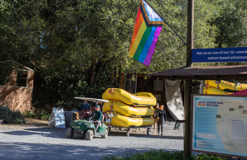 A pride flag hangs at the American River Outpost as a group of guides move three yellow rafts on a trailer