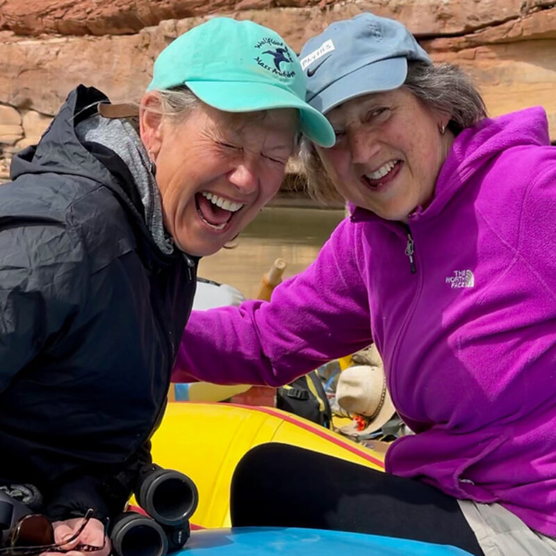 Two laughing women pose for a photo while sitting on a yellow raft on the Colorado River