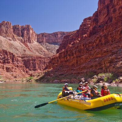 A yellow oar raft with people rowing down an emerald Colorado River in Grand Canyon