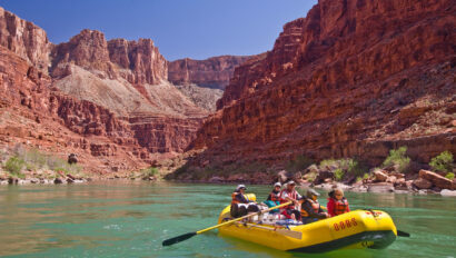 A yellow oar raft with people rowing down an emerald Colorado River in Grand Canyon