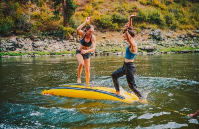 Two women play a balance game on a upside-down inflatable kayak floating in the Main Salmon River