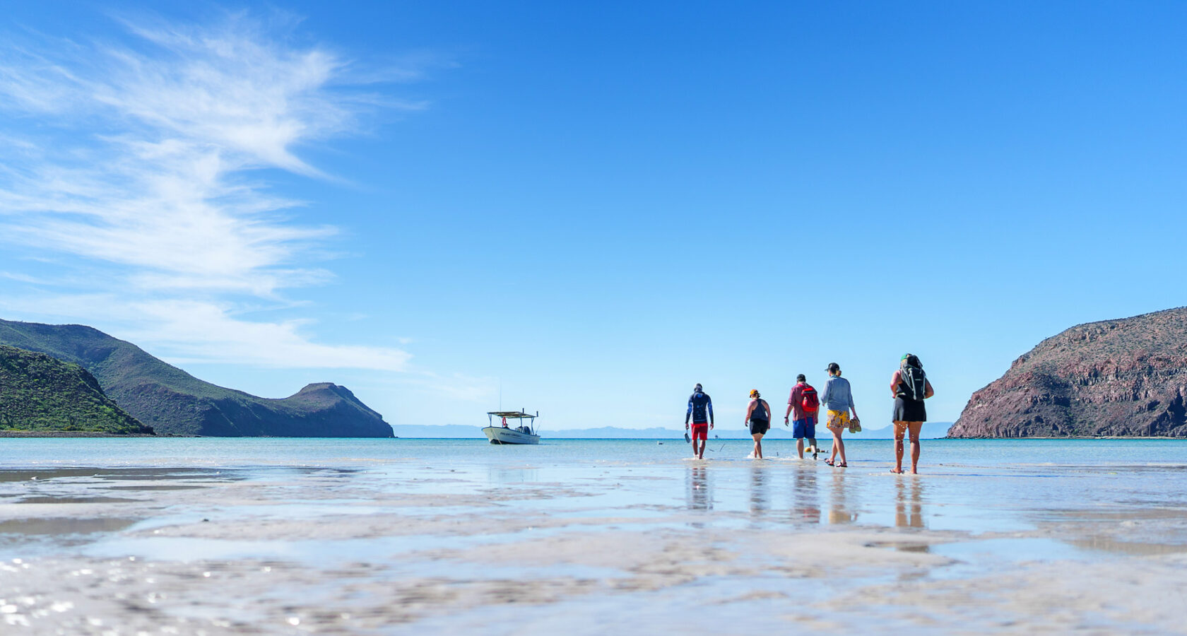 A group walks in shallow water off toward a boat in Baja, Mexico