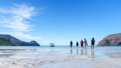 A group walks in shallow water off toward a boat in Baja, Mexico