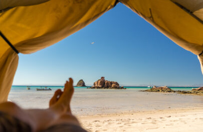 View of the ocean taken from inside a tent on a sandy beach in Baja Mexico as a guest kicks their feet up to relax