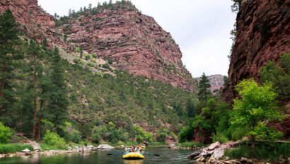 Scenic shot of yellow rafts coming down the Green River surounded by lush greenery and canyon walls