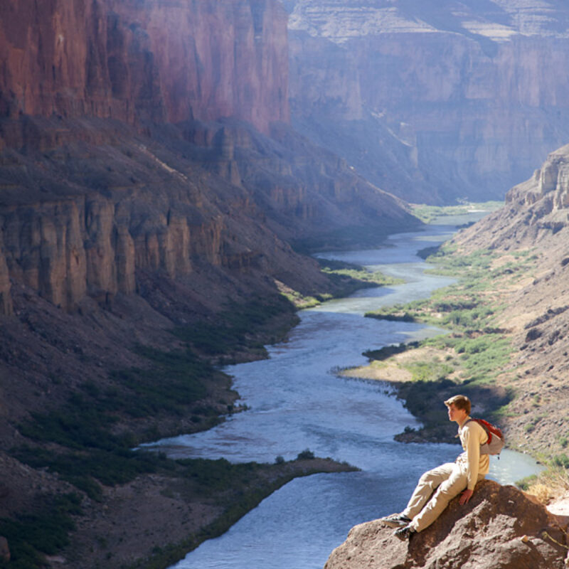 A hiker sits on a rock and takes in the view high above the Colorado River in Grand Canyon