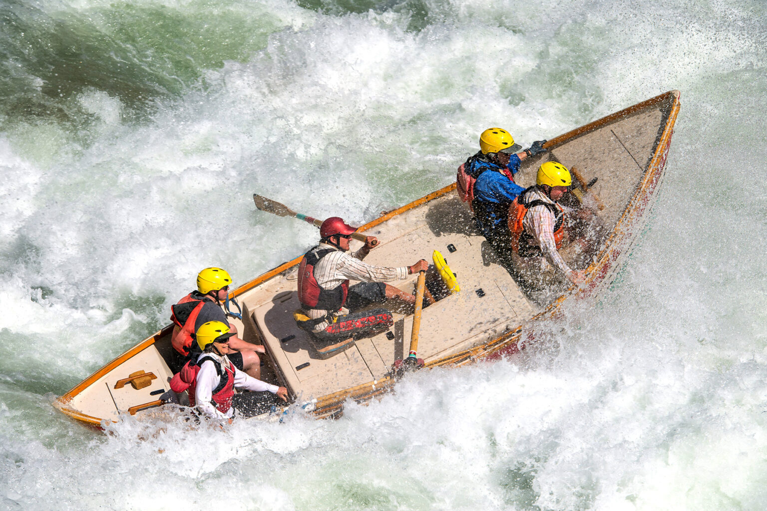 A dory rowed by a guide with four guests crashes through a frothy rapid on the Colorado River in Grand Canyon