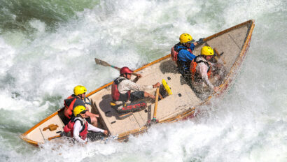 A dory rowed by a guide with four guests crashes through a frothy rapid on the Colorado River in Grand Canyon