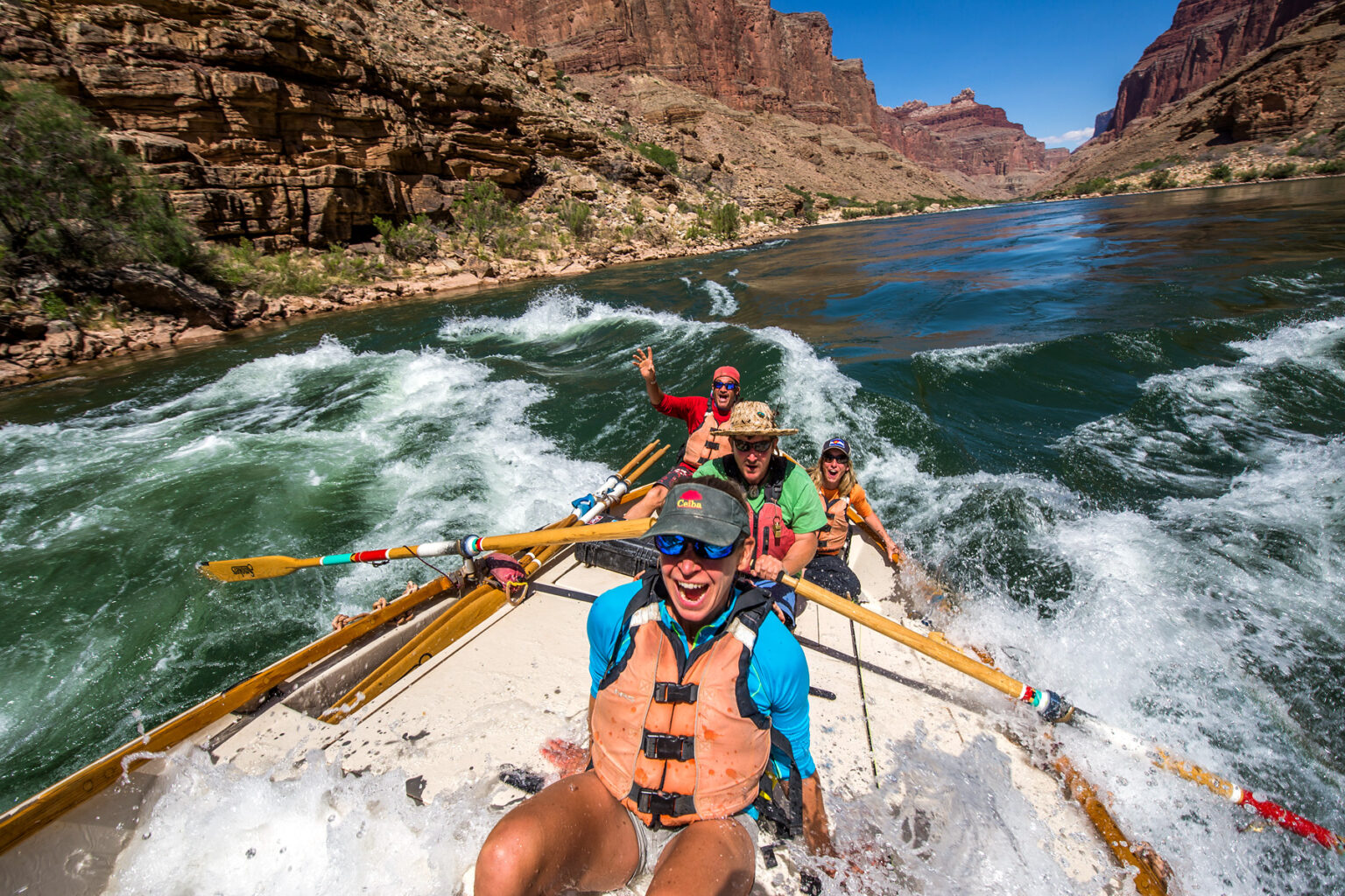 A dory rowed by a guide with three guests as they go through a rapid on the Colorado River in Grand Canyon
