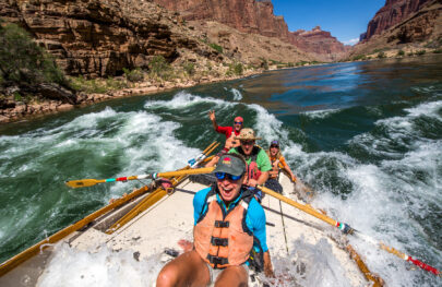 A dory rowed by a guide with three guests as they go through a rapid on the Colorado River in Grand Canyon