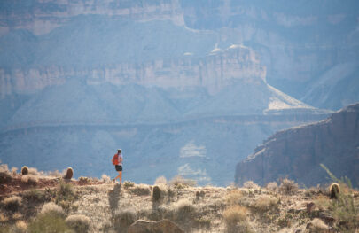 Lone hiker with backpack hikes along rim trail with cactus and breathtaking views