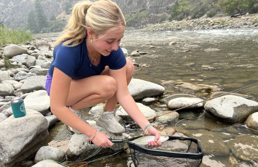 A fly fisherwoman holds a trout at the edge of the Middle Fork Salmon River in Idaho during a rafting trip