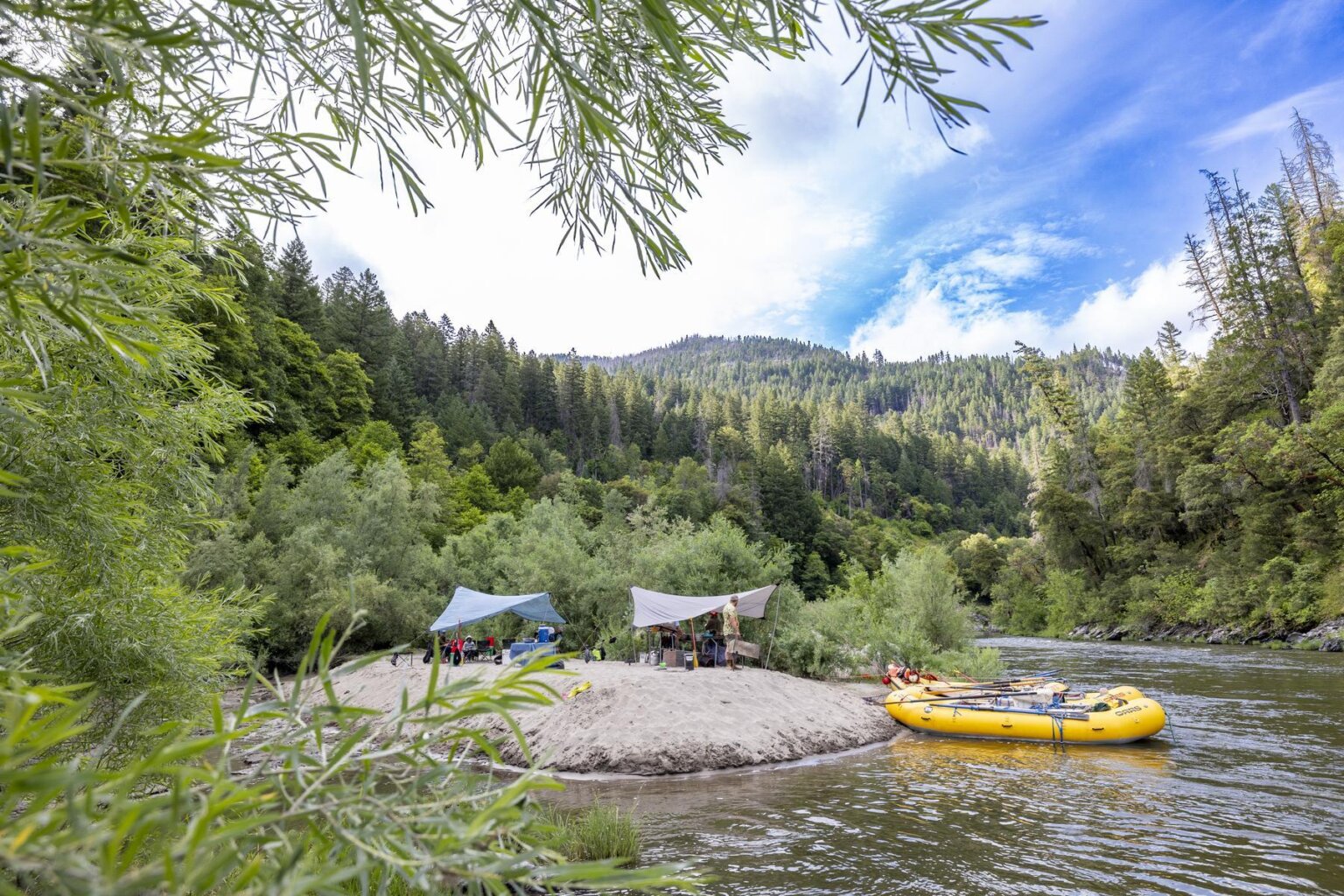 A camp site with OARS yellow rafts on the right on the Klamath River in Northern California.