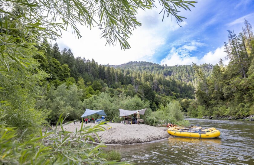A camp site with OARS yellow rafts on the right on the Klamath River in Northern California.