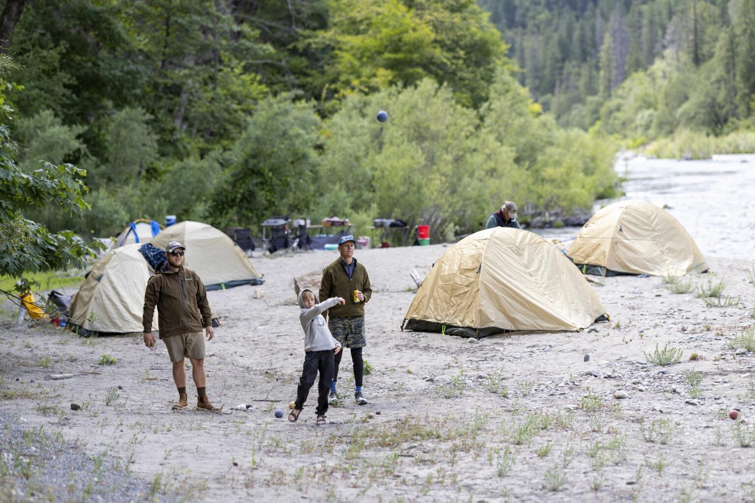 Two adults and a boy play bocci ball on a beach on the Klamath River during a rafting trip with OARS.