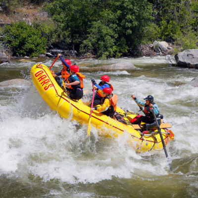 The nose of a yellow raft up in the air as a group of paddlers take on a rapid on the Merced River in California