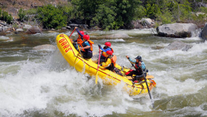 The nose of a yellow raft up in the air as a group of paddlers take on a rapid on the Merced River in California