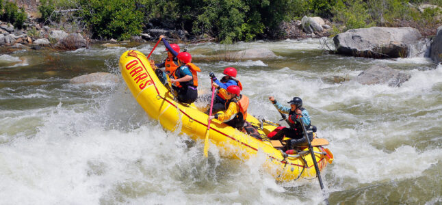 The nose of a yellow raft up in the air as a group of paddlers take on a rapid on the Merced River in California