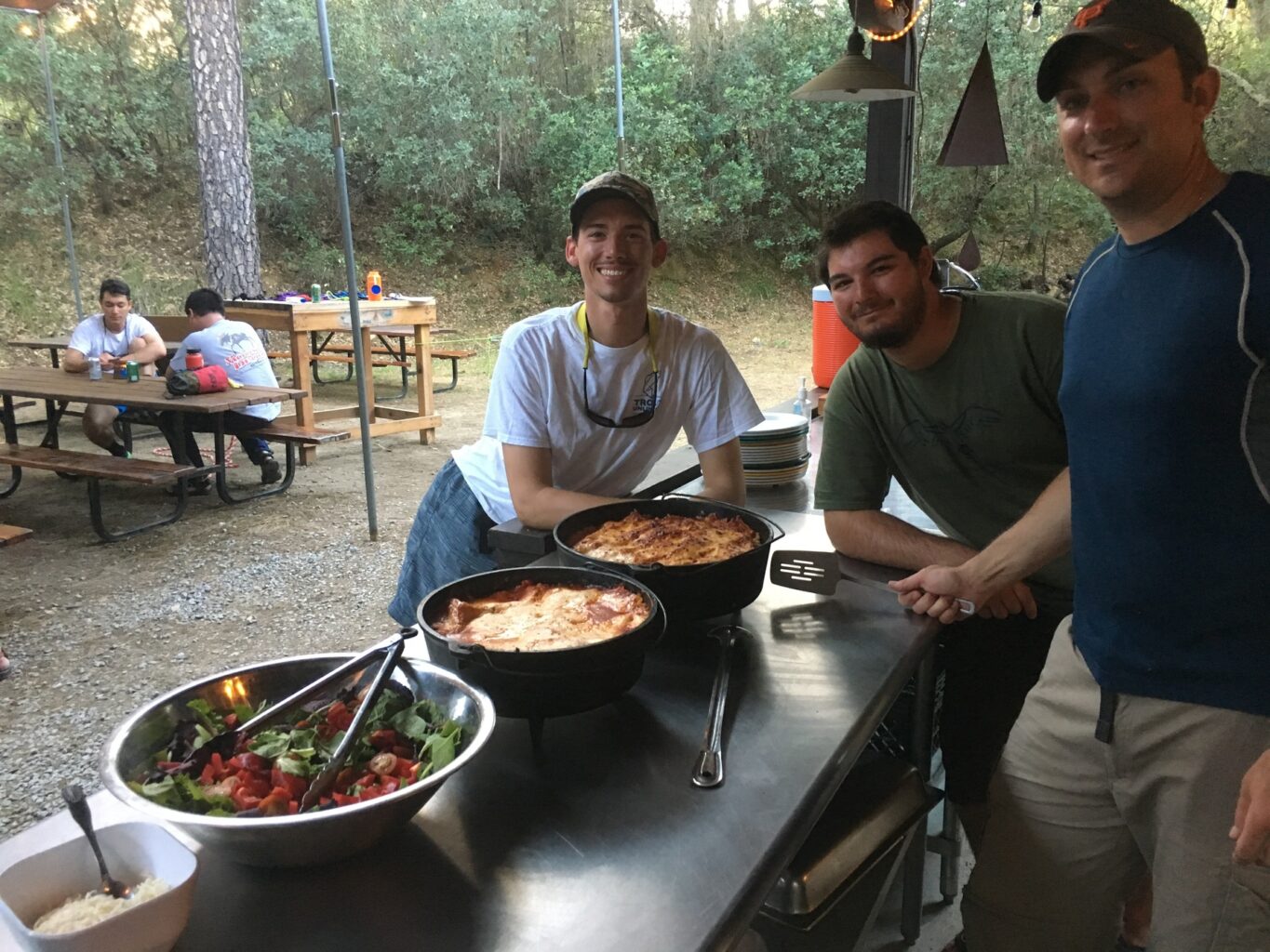 Three male guides in training stand around food they prepared during OARS California guide school