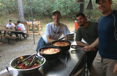 Three male guides in training stand around food they prepared during OARS California guide school