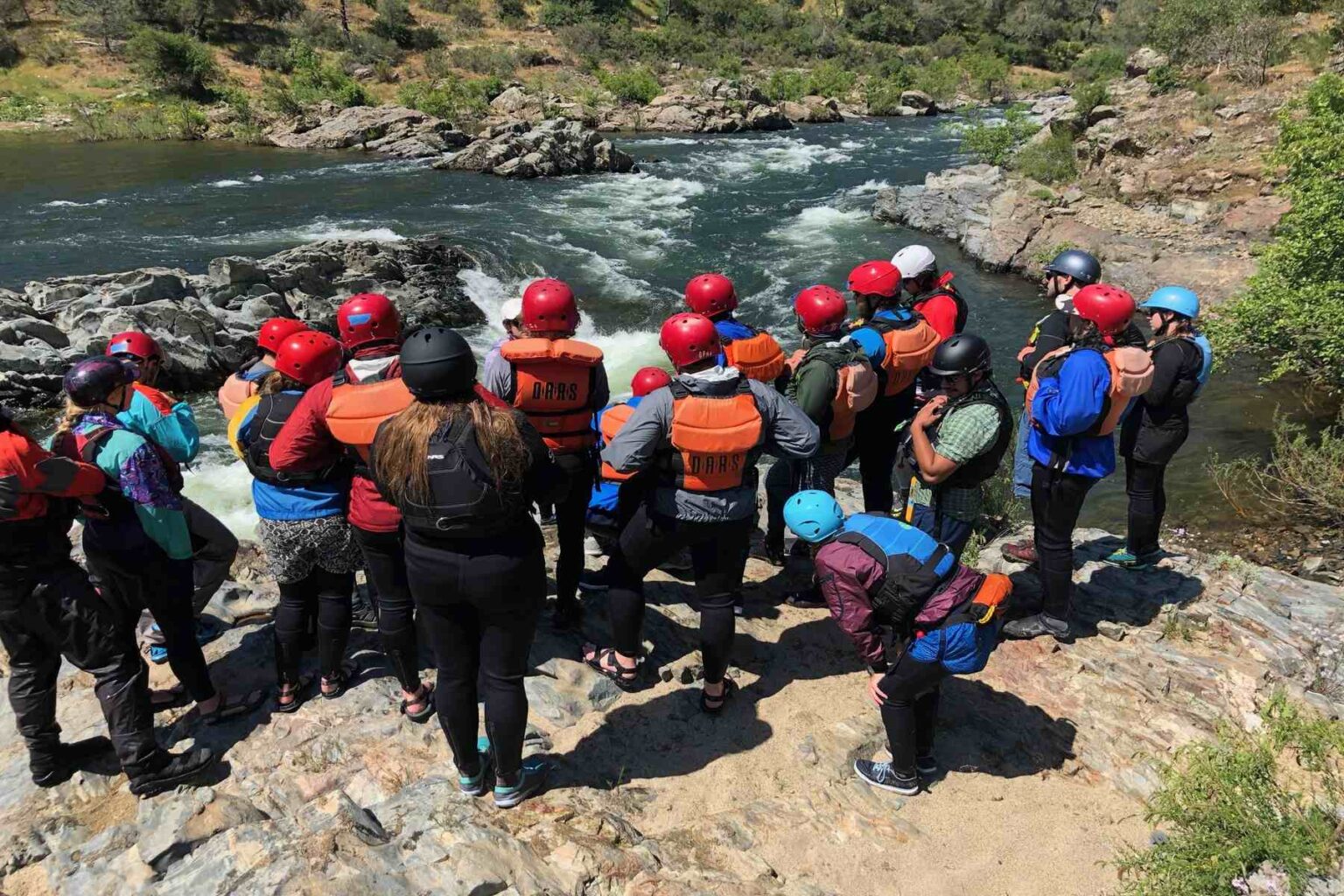 Participants in OARS California guide school scout Satans Cesspool rapid on the American River from shore.