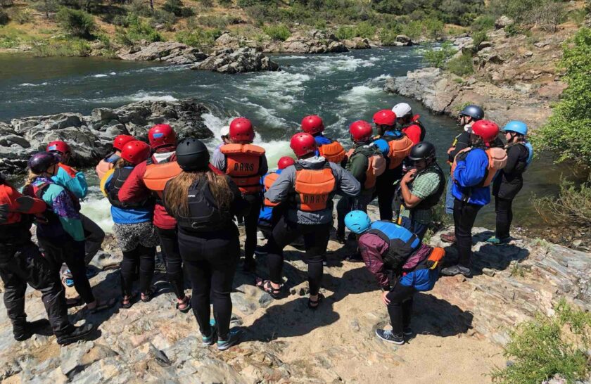 Participants in OARS California guide school scout Satans Cesspool rapid on the American River from shore.
