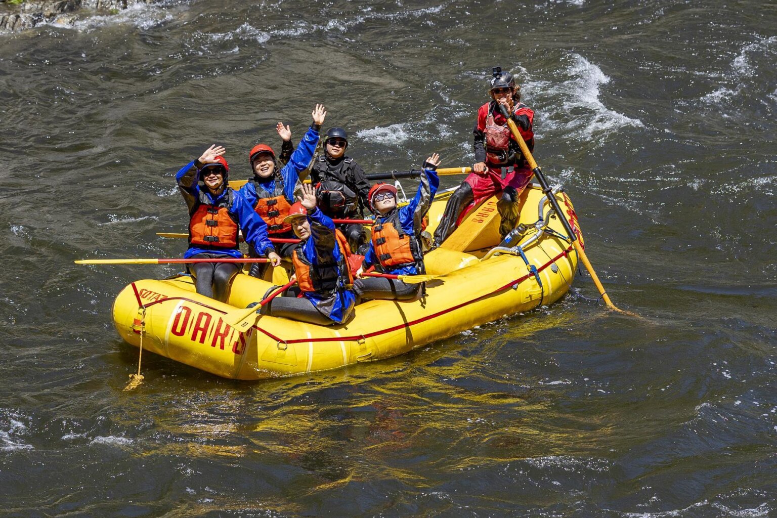A group of rafters waves during a raft trip on the Merced River in May 2025.