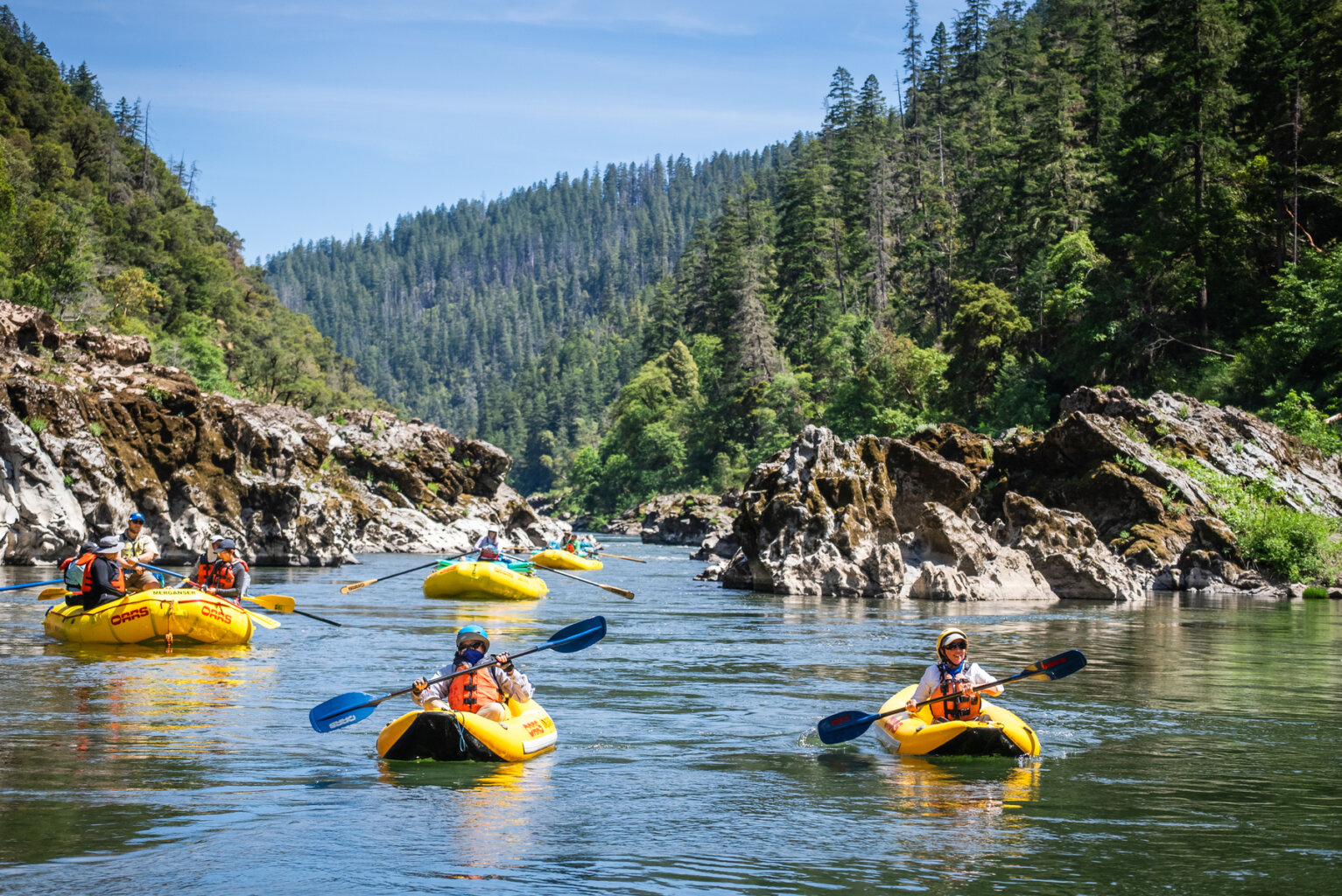 A group on yellow rafts and inflatable kayaks floats on the Rogue River in Oregon during an OARS rafting trip in 2025.