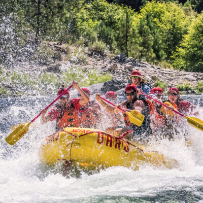 A raft full of people paddle through whitewater as spray surrounds the boat