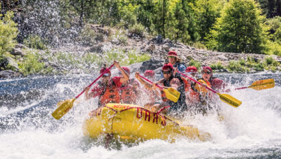 A raft full of people paddle through whitewater as spray surrounds the boat