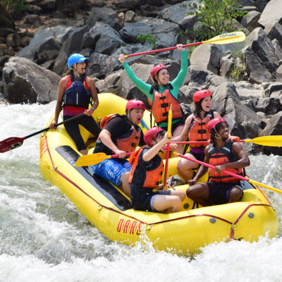 A paddle raft full of smiling happy people going through a rapid on the South Fork of the American River