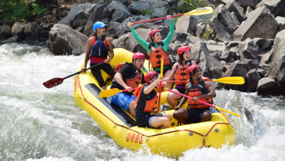 A paddle raft full of smiling happy people going through a rapid on the South Fork of the American River