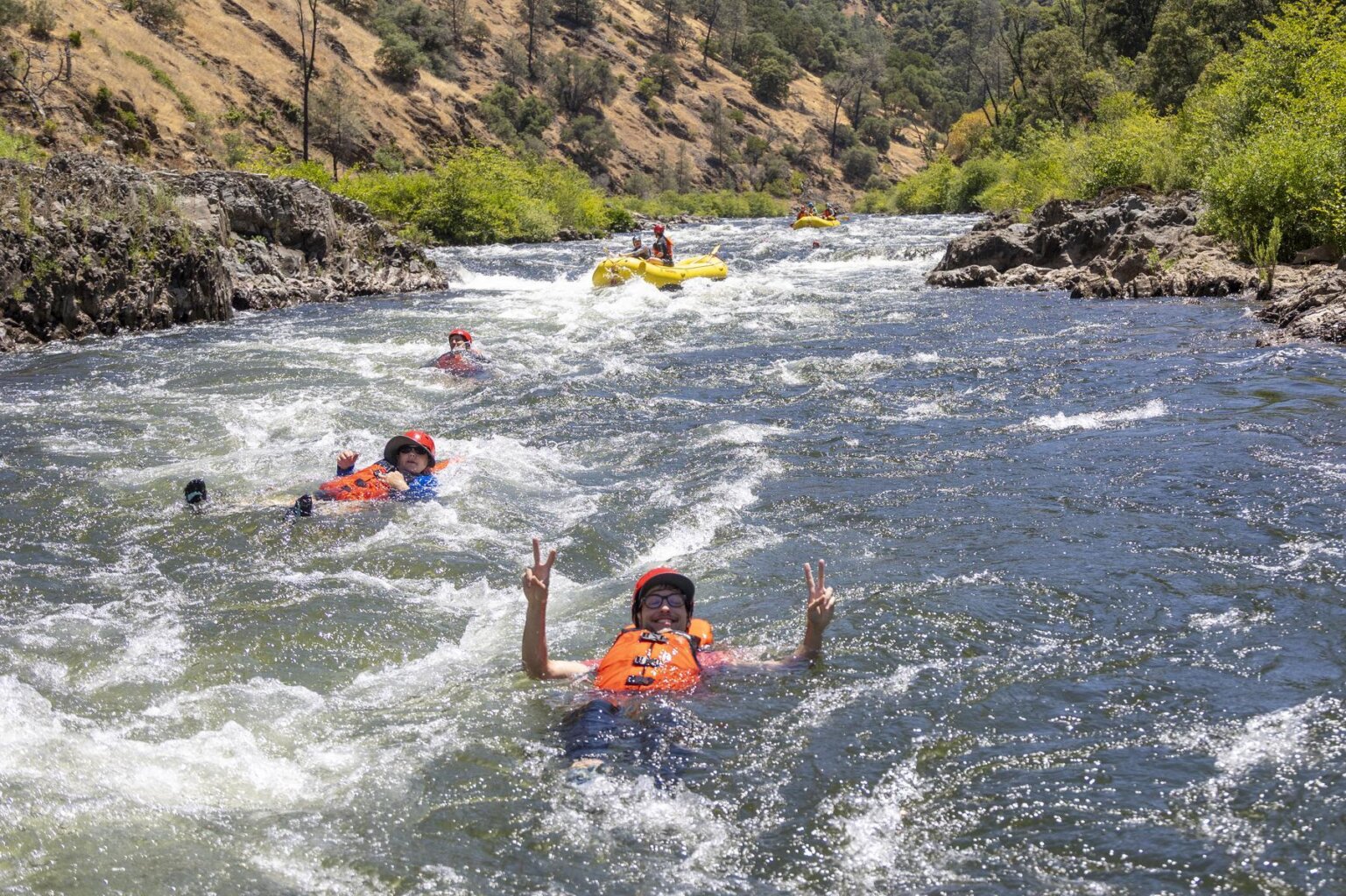 Swimmers in orange life jackets float down a rapid on the South Fork of the American River during an OARS whitewater guide school in California.