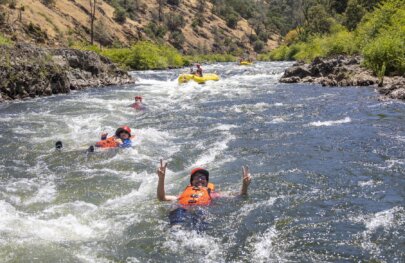 Swimmers in orange life jackets float down a rapid on the South Fork of the American River during an OARS whitewater guide school in California.
