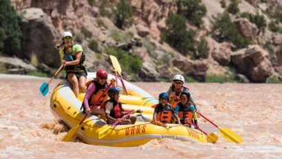 Three children sit in the front of a paddle raft with two adults and a guide behind them all smiling and having a blast on the Green River through Split Mountain Canyon