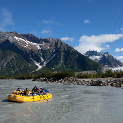 A yellow raft on the Tatshenshini River with mountains behind in Alaska