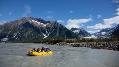 A yellow raft on the Tatshenshini River with mountains behind in Alaska