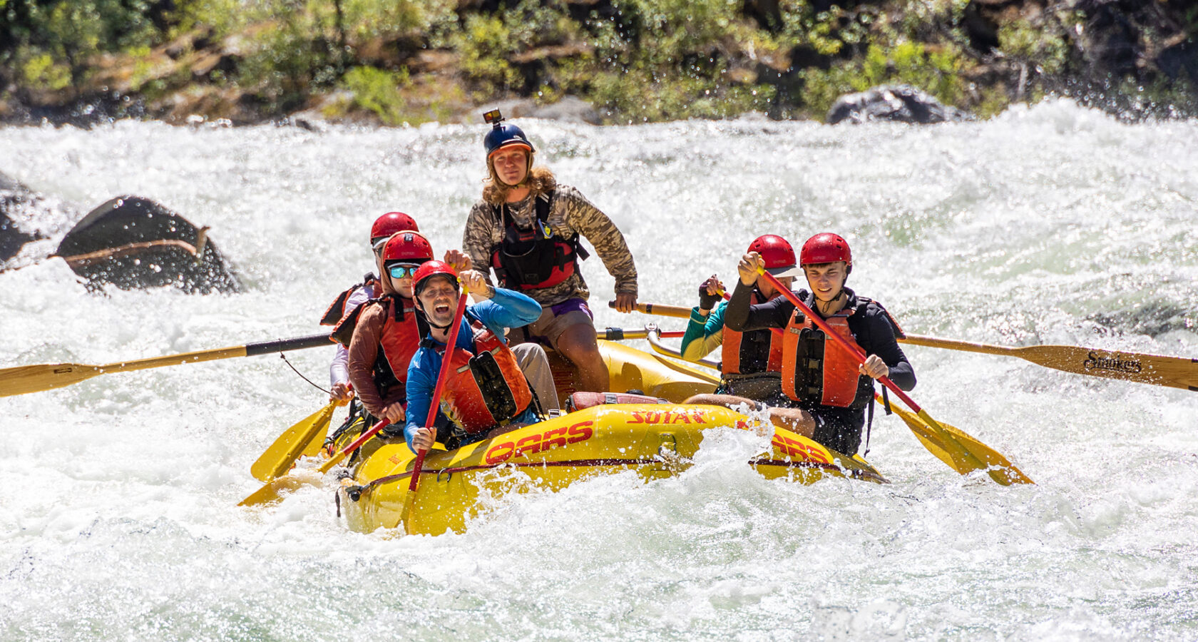 A yellow raft of paddlers surounded by frothy whitewater as they make their way through a rapid on the Tuolumne River in California