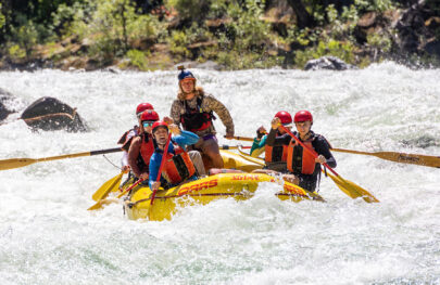 A yellow raft of paddlers surounded by frothy whitewater as they make their way through a rapid on the Tuolumne River in California