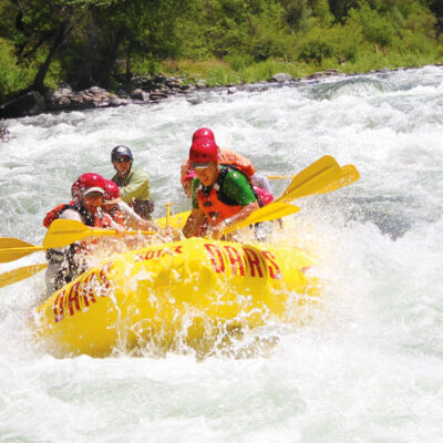 A yellow raft of paddlers surounded by frothy whitewater as they make their way through a rapid on the Tuolumne River in California