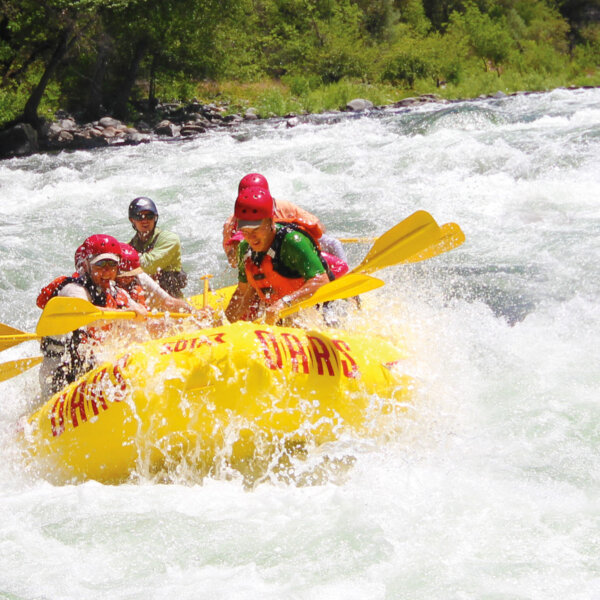 A yellow raft of paddlers surounded by frothy whitewater as they make their way through a rapid on the Tuolumne River in California