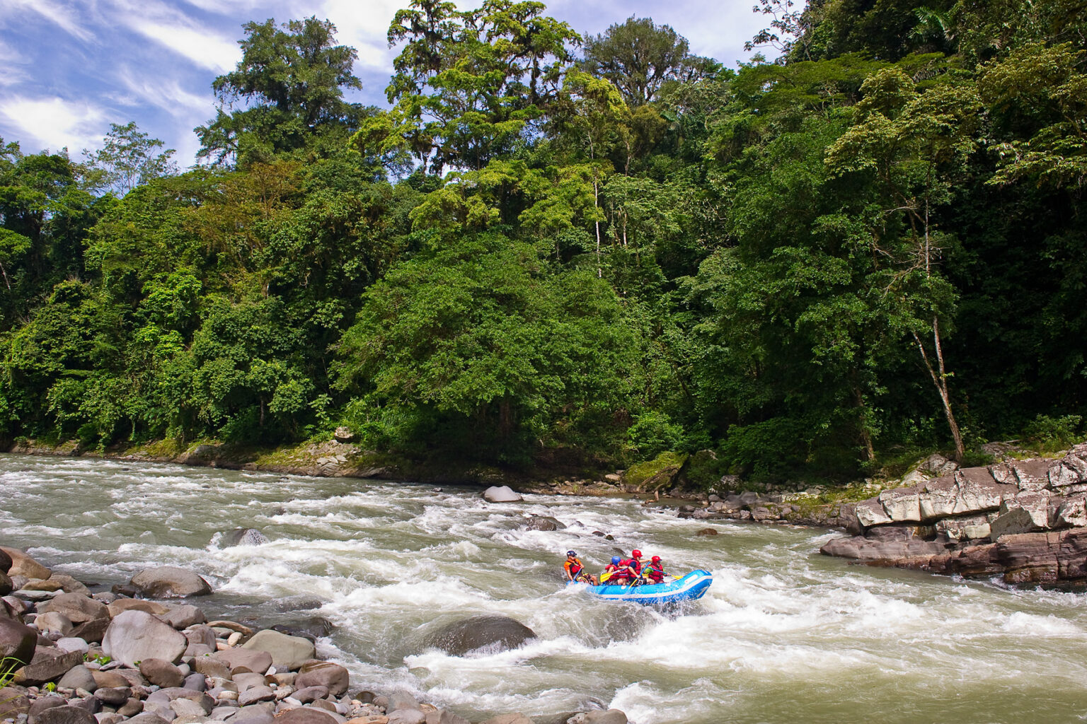 A paddle raft going through rapids surrounded by lush rainforest on a Costa Rica Pura Vida trip