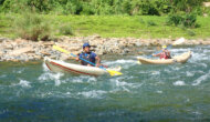 Guests in two inflatable kayaks paddle down the Middle Navua with green rainforest behind them.